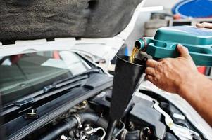 tema de reparação e manutenção de automóveis. mecânico de uniforme trabalhando em auto serviço, derramando óleo de motor novo. foto