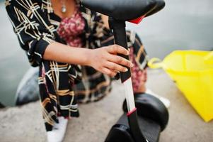 linda mulher afro-americana sente-se perto de segway ou hoverboard. garota negra com símbolo de reciclagem de sacos ecológicos de pano amarelo. foto