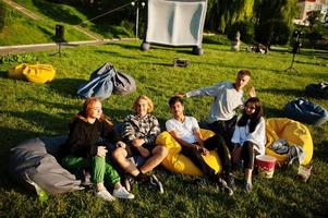 jovem grupo multiétnico de pessoas assistindo filme no poof no cinema ao ar livre. foto