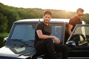 dois irmãos asiáticos vestem todo preto posando perto do carro suv. foto