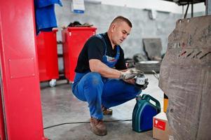 tema de reparação e manutenção de automóveis. mecânico de uniforme trabalhando em auto serviço, derramando óleo de motor novo. foto