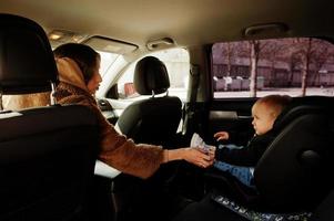 jovem mãe e filho no carro. assento de bebê na cadeira. conceito de condução de segurança. foto