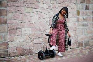 linda mulher afro-americana fica perto de segway ou hoverboard. garota negra com scooter elétrico de auto balanceamento de roda dupla. foto