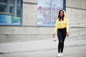 garota afro-americana hipster vestindo capuz amarelo posando na rua. foto