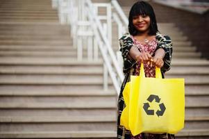 linda mulher afro-americana com símbolo de reciclagem de sacos ecológicos de pano amarelo. foto