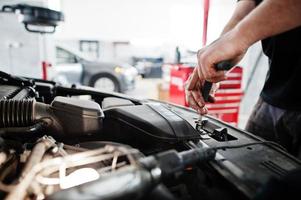 tema de reparação e manutenção de automóveis. mecânico de uniforme trabalhando em auto serviço, verificando o motor. foto