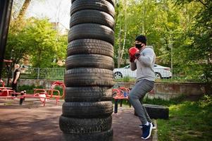 retrato esportivo homem boxer árabe em máscara facial médica preta boxe ao ar livre durante a quarentena de coronavírus. foto