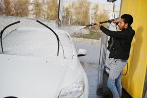 homem do sul da Ásia ou homem indiano lavando seu transporte branco na lavagem de carros. foto