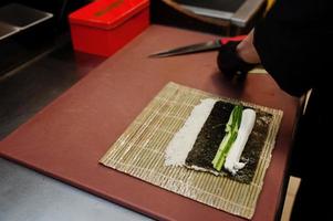 Feche as mãos do chef profissional vestindo luvas pretas fazendo sushi e pãezinhos em uma cozinha de restaurante de comida tradicional japonesa. foto