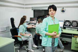 .portrait de tema médico de médica com prancheta contra grupo de médicos reunidos no escritório de ressonância magnética no centro de diagnóstico no hospital. foto