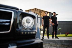 dois irmãos asiáticos vestem todo preto posando perto do carro suv. foto