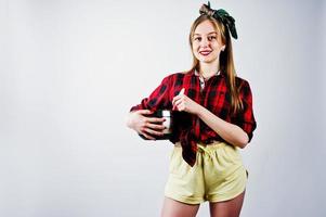 jovem dona de casa engraçada na camisa quadriculada e short amarelo pin up estilo com panela e colher de cozinha isolado no fundo branco. foto