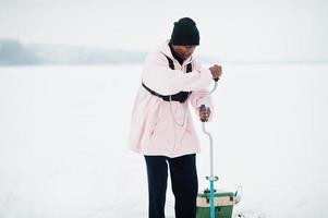 pescador americano africano fazendo buraco no gelo congelado por broca. pesca de inverno. foto