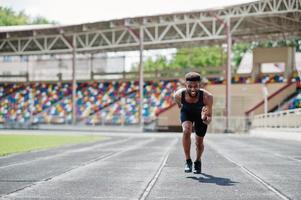 atleta masculino americano africano em roupas esportivas correndo sozinho em uma pista de corrida no estádio. foto