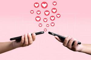 as pessoas usam o celular enviando coração umas para as outras. conceito de amor e conexão usando aplicativo de telefone em fundo rosa. foto