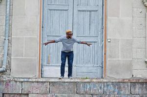 menino afro-americano elegante na camisola cinza e óculos de sol pretos posou na rua. salto de cara preto na moda. foto