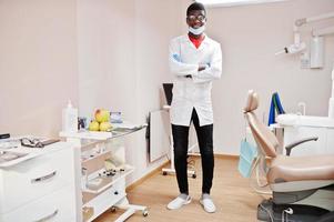 médico americano africano em óculos e máscara posou na clínica com os braços cruzados. foto
