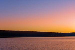 vívido pôr do sol laranja sobre montanhas e águas calmas foto