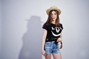 retrato de uma garota atraente em t-shirt preta dizendo lol, shorts jeans, chapéu e óculos de sol posando no estúdio. foto