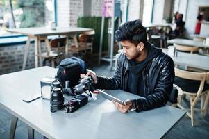 fotógrafo de jovem asiático inteligente trabalhando com tablet durante a sessão no café. foto
