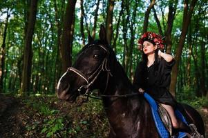 garota mística em grinalda veste de preto a cavalo em madeira. foto