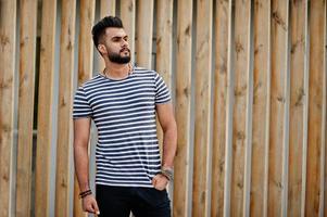 modelo de homem de barba árabe alto bonito na camisa despojada posou ao ar livre contra um fundo de madeira. cara árabe na moda. foto