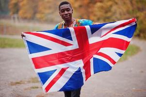 homem africano na camisa tradicional da África no parque outono com bandeira da Grã-Bretanha. foto