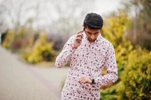 estudante indiano na camisa posou ao ar livre, falando no telefone e olhando para seus relógios. foto