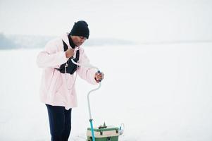 pescador americano africano fazendo buraco no gelo congelado por broca. pesca de inverno. foto