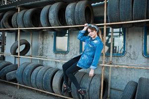 garota jovem hippie na jaqueta jeans e lenço na cabeça na zona de montagem do pneu. foto