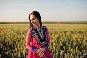 tenra garota indiana em saree, com lábios violeta compõem posou no campo no pôr do sol. modelo elegante da índia. foto