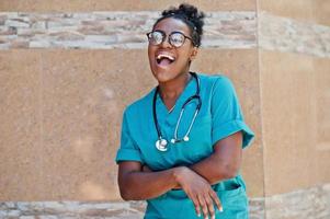 médico americano africano feminino no jaleco com estetoscópio posado ao ar livre contra a clínica. foto