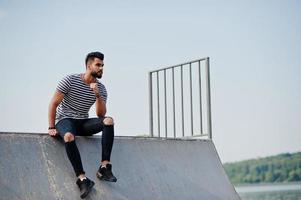 modelo de homem de barba árabe alto bonito na camisa despojada posou ao ar livre no skate park. cara árabe na moda. foto