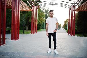 homem de barba indiana elegante na camiseta rosa. modelo da índia posou sob o arco vermelho no parque da cidade. foto