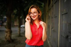 mulher ruiva atraente em óculos, use blusa vermelha e saia jeans posando. foto