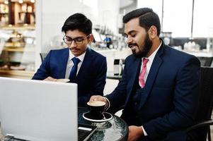 dois homens de negócios indianos de terno sentado no escritório no café, olhando para o laptop e tomando café. foto