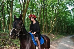 garota mística em grinalda veste de preto a cavalo em madeira. foto