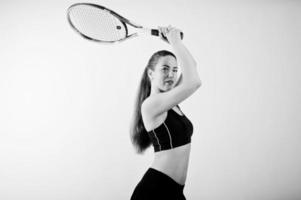 retrato preto e branco do jogador de mulher jovem e bonita em roupas esportivas, segurando a raquete de tênis em pé contra um fundo branco. foto