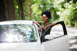 mulher afro-americana posou contra carro branco na estrada florestal. foto