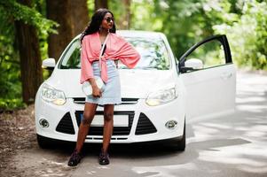 mulher afro-americana posou contra carro branco na estrada florestal. foto