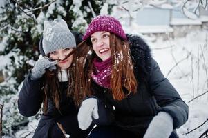 duas amigas engraçadas se divertindo no dia de inverno nevado perto de árvores cobertas de neve. foto