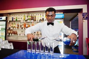 barman americano africano no bar fazendo coquetéis em tiros. preparação de bebidas alcoólicas. foto