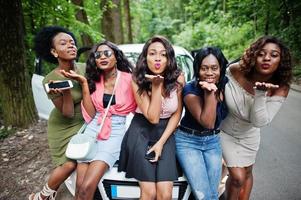 grupo de cinco garotas afro-americanas felizes sentadas em um capô de carro. foto