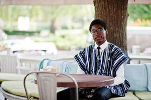 homem africano em roupas tradicionais e óculos sentados no caffe ao ar livre. foto