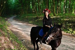 garota mística em grinalda veste de preto a cavalo em madeira. foto