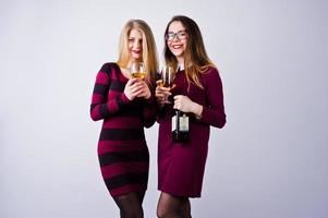 duas amigas atraentes em vestidos roxos bebem vinho espumante ou champanhe no estúdio. foto