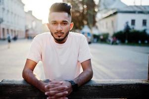 homem de barba indiana elegante na camiseta rosa. modelo da índia posou ao ar livre nas ruas do pôr do sol da cidade. foto