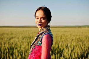 tenra garota indiana em saree, com lábios violeta compõem posou no campo no pôr do sol. modelo elegante da índia. foto