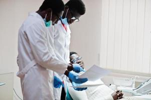 paciente de homem afro-americano na cadeira odontológica. consultório de dentista e conceito de prática médica. dentista profissional ajudando seu paciente na odontologia médica. apontando para o raio-x dos dentes. foto