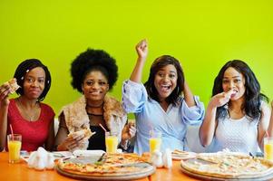 quatro jovens garotas africanas no restaurante colorido brilhante comendo pizza e se divertindo juntos. foto